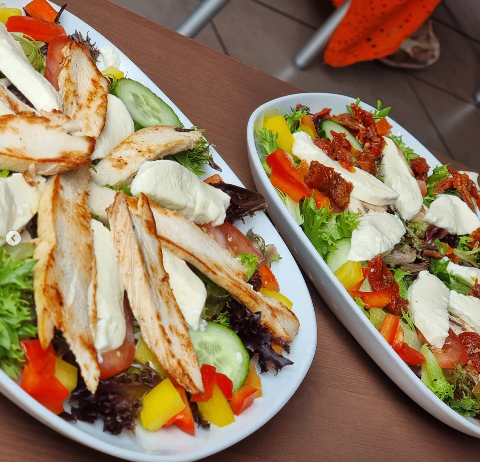 Two fresh chicken and mozzarella salad platters with peppers, cucumber and sun-dried tomatoes