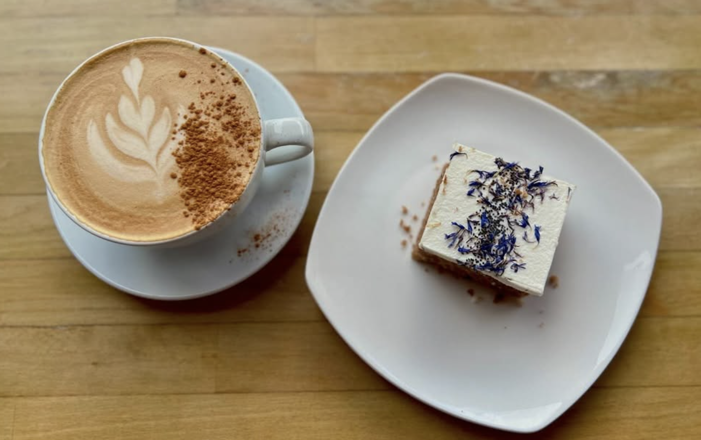 Cappuccino with latte art beside a slice of cake topped with edible flowers