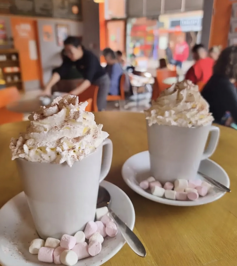 Two hot chocolates topped with whipped cream and marshmallows in the cafe